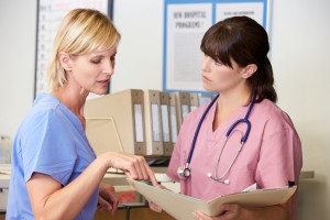 Two,Nurses,Discussing,Patient,Notes,At,Nurses,Station